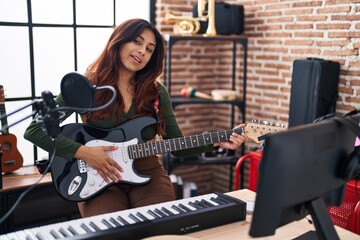 Obraz na płótnie Canvas Young hispanic woman artist playing electrical guitar at music studio