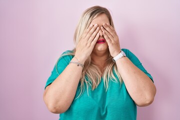 Caucasian plus size woman standing over pink background rubbing eyes for fatigue and headache,...