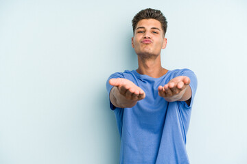 Young caucasian man isolated on blue background folding lips and holding palms to send air kiss.