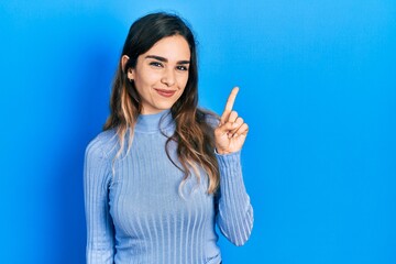 Young hispanic girl wearing casual clothes showing and pointing up with finger number one while smiling confident and happy.