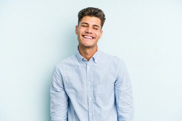 Young caucasian man isolated on blue background laughs and closes eyes, feels relaxed and happy.