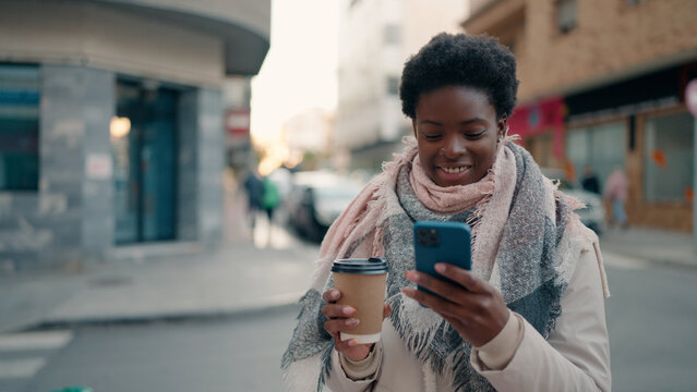 Young african american woman using smartphone drinking coffee at street
