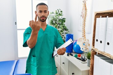 African american physiotherapist man working at pain recovery clinic showing middle finger, impolite and rude fuck off expression