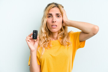 Young caucasian woman holding car keys isolated on blue background being shocked, she has remembered important meeting.