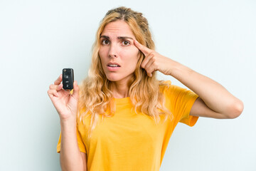 Young caucasian woman holding car keys isolated on blue background showing a disappointment gesture with forefinger.