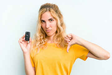 Young caucasian woman holding car keys isolated on blue background showing a dislike gesture, thumbs down. Disagreement concept.