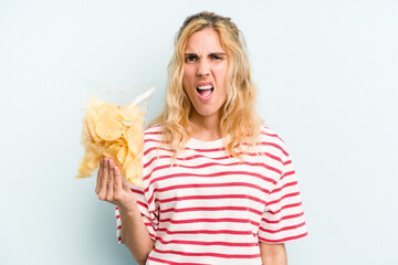 Young caucasian woman holding a bag of chips isolated on blue background screaming very angry and...