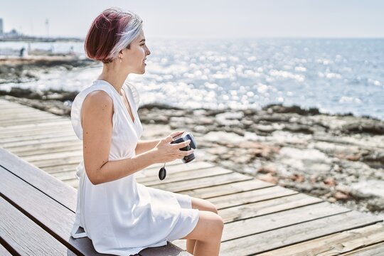 Young caucasian girl using professional camera sitting on the bench at the beach.