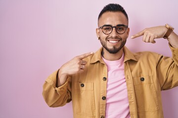 Fototapeta premium Young hispanic man standing over pink background smiling cheerful showing and pointing with fingers teeth and mouth. dental health concept.