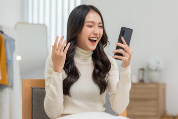 Millennial asian young woman looking mobile phone laughing with good news or discount voucher for...