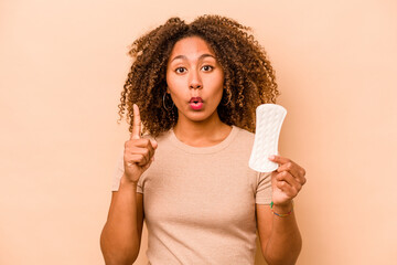 Young African American woman holding sanitary napkin isolated on beige background having some great idea, concept of creativity.