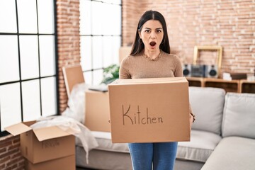 Young woman moving to a new home holding box afraid and shocked with surprise and amazed expression, fear and excited face.