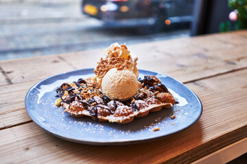  Plate of waffle with chocolate sauce and ice cream on wooden surface