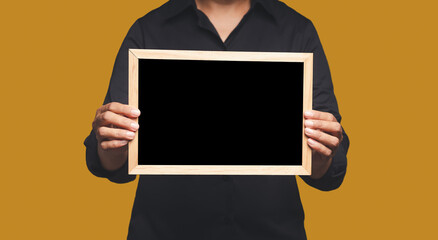 Close-up of hands holding a blank mini blackboard while standing on an orange background. Space for text