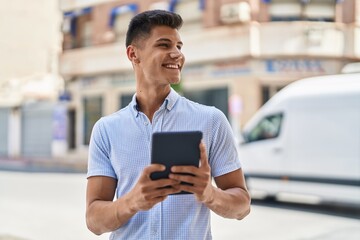 Young hispanic man smiling confident using touchpad at street