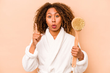 Young African American woman holding back scratcher isolated on beige background having some great idea, concept of creativity.