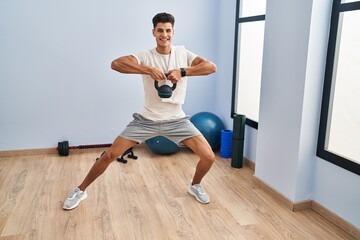 Fototapeta na wymiar Young hispanic man smiling confident training using kettlebell at sport center