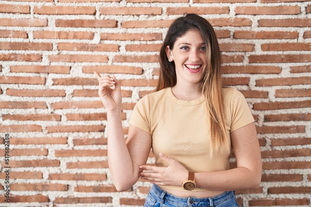 Sticker young brunette woman standing over bricks wall with a big smile on face, pointing with hand finger t