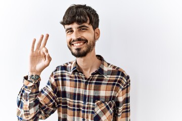 Hispanic man with beard standing over isolated background smiling positive doing ok sign with hand and fingers. successful expression.