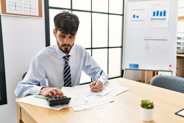 Young hispanic businessman with serious expression working at the office.