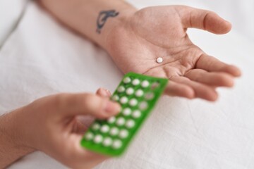 Young woman holding birth control pills at bedroom
