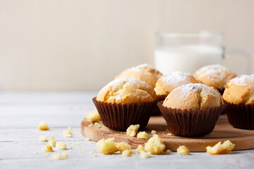 Tasty sweet breakfast, homemade cakes. Freshly baked homemade muffins in brown paper cups and glass of milk on white wooden table.