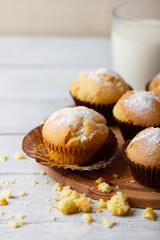 Tasty sweet breakfast, homemade cakes. Freshly baked homemade muffins in brown paper cups and glass of milk on white wooden table.