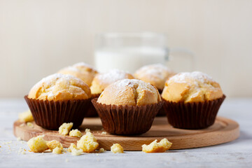 Tasty sweet breakfast, homemade cakes. Freshly baked homemade muffins in brown paper cups and glass of milk on white wooden table.