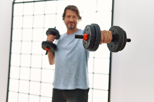 Middle age caucasian man smiling confident training using dumbbells at sport center