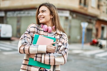 Young blonde woman wearing headphones smiling confident holding books at street