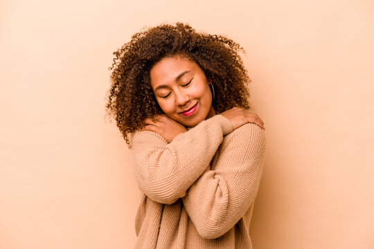 Young African American woman isolated on beige background hugs, smiling carefree and happy.