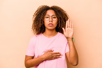 Young African American woman isolated on beige background taking an oath, putting hand on chest.