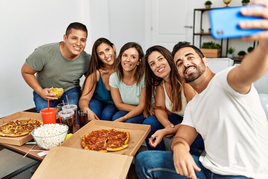 Group of young hispanic friends eating italian pizza make selfie. by the smartphone at home.