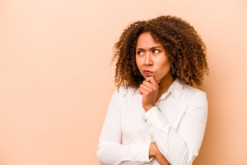 Young African American woman isolated on beige background looking sideways with doubtful and skeptical expression.