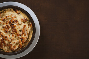 Mushroom and meat casserole covered with melted cheese and served in a dark dish on the table