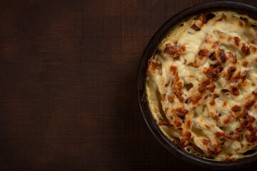 Mushroom and meat casserole covered with melted cheese and served in a dark dish on the table
