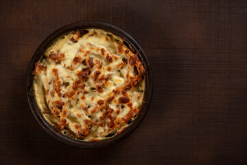 Mushroom and meat casserole covered with melted cheese and served in a dark dish on the table