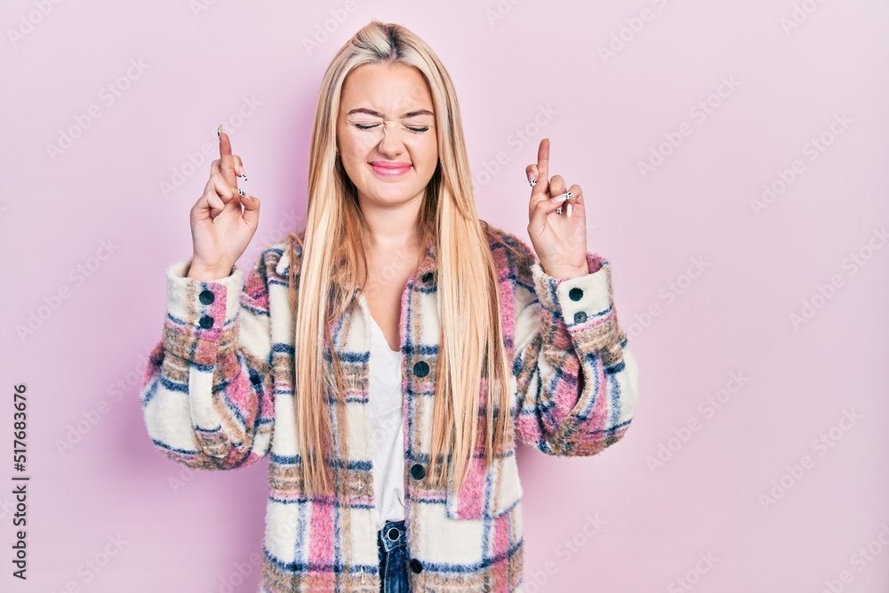 Wall mural young blonde girl wearing casual clothes gesturing finger crossed smiling with hope and eyes closed.