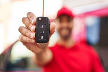 Young hispanic man courier holding car key at street