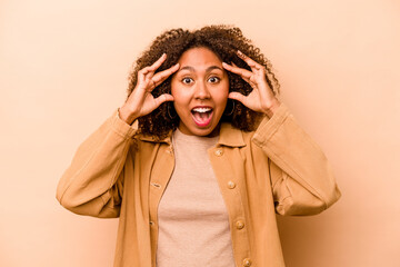 Young African American woman isolated on beige background receiving a pleasant surprise, excited and raising hands.