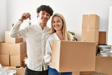 Fototapeta na wymiar Young beautiful couple smiling happy holding cardboard box and key of new home.