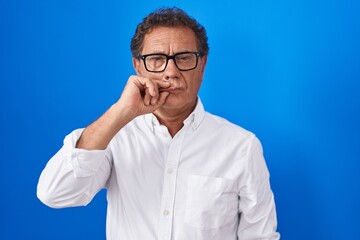 Middle age hispanic man standing over blue background mouth and lips shut as zip with fingers. secret and silent, taboo talking