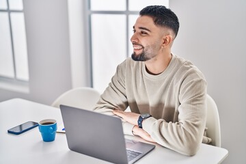 Young arab man using laptop and drinking coffee sitting on table at home