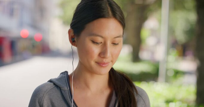 Portrait of active young woman listening to music or podcast on earphones in busy urban city after gym workout. Closeup headshot or face of determined, cool or confident woman enjoying songs in town