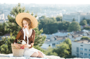 Young girl in a straw hat, posing against the background of the city from an observation deck.