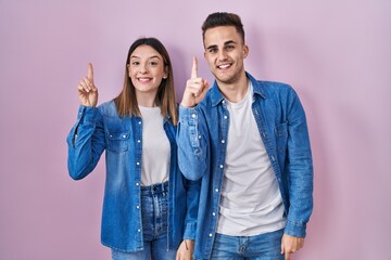 Fototapeta premium Young hispanic couple standing over pink background pointing finger up with successful idea. exited and happy. number one.
