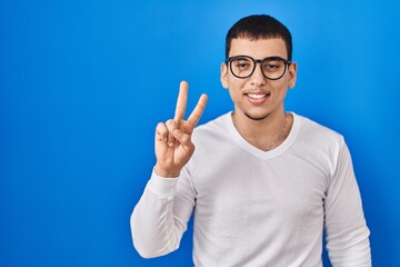 Young arab man wearing casual white shirt and glasses showing and pointing up with fingers number two while smiling confident and happy.