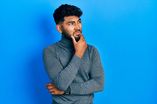 Arab man with beard wearing turtleneck sweater thinking worried about a question, concerned and nervous with hand on chin