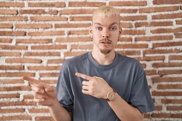 Young caucasian man standing over bricks wall pointing aside worried and nervous with both hands,...