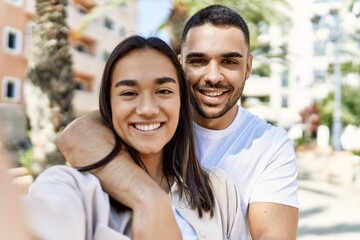 Young latin couple smiling happy and hugging making selfie by the camera at the city.